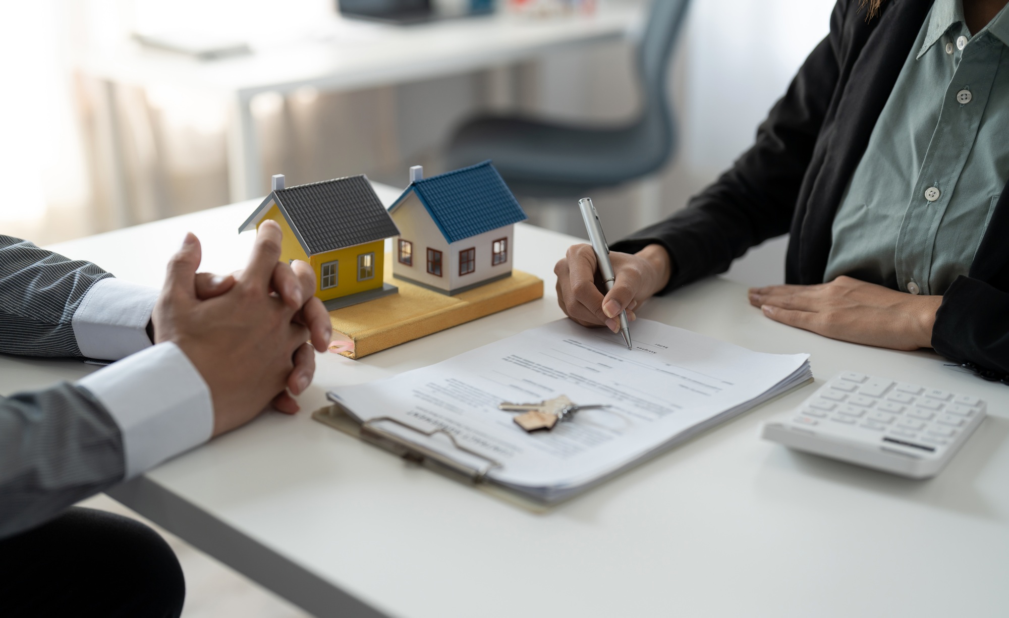 Real estate agent assisting client to sign contract at desk with house model